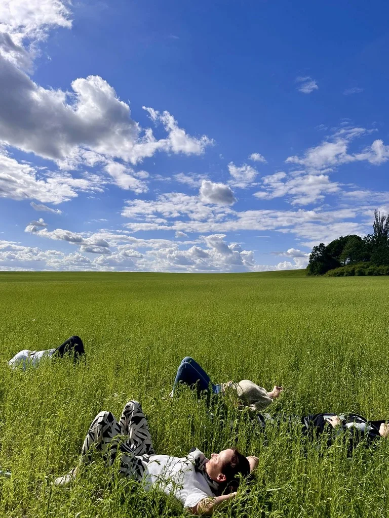 Frauen liegen im hohen Gras unter einem weiten Sommerhimmel.