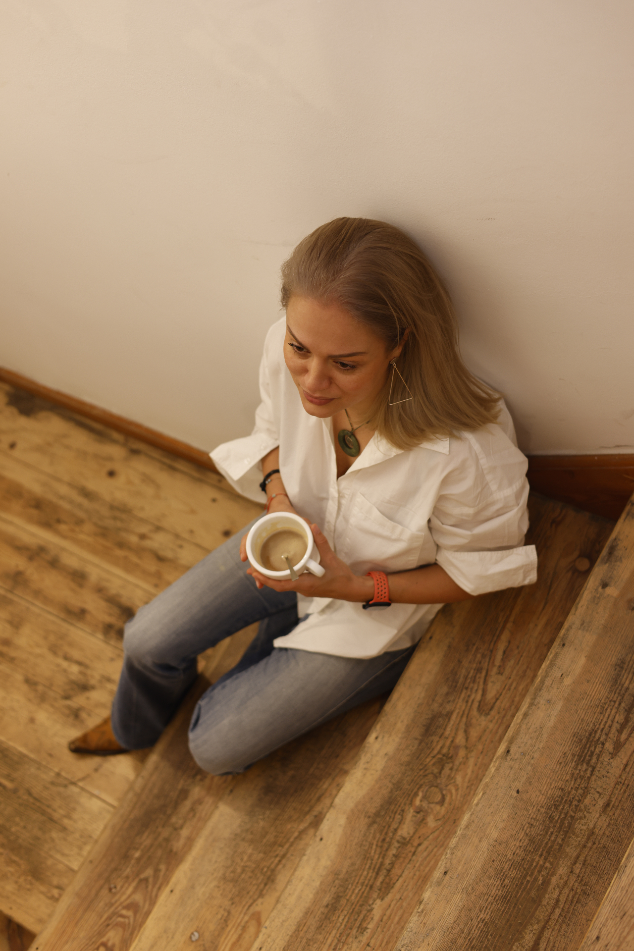 Alissa Rentowitsch sitzt mit einer Tasse Kaffee auf einer Holztreppe.